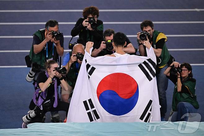 우상혁이 21일(현지시간) 중국 난징 유스올림픽스포츠파크에서 열린 2025 세계 실내 육상 선수권 대회 남자 높이뛰기서 2m31을 넘어 3년 만에 우승을 한 뒤 태극기를 두르며 취재진에 포즈를 취하고 있다. 2025.03,22 ⓒ AFP=뉴스1 ⓒ News1 우동명 기자