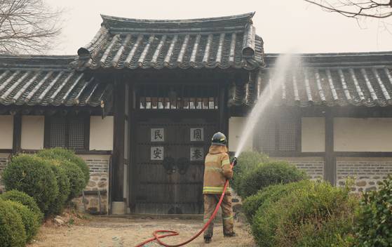 A firefighter sprays water on a building in Hahoe Folk Village in Andong, North Gyeongsang, on March 26. The village, which is a Unesco-designated World Heritage Site, is located near one of the wildfires ravaging southeastern Korea. [YONHAP]