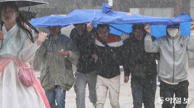 14일 오전 서울 종로구 경복궁에서 외국인 관광객들이 우비 하나를 함께 쓴 채 비를 피하고 있다. 송은석 기자 silverstone@donga.com
