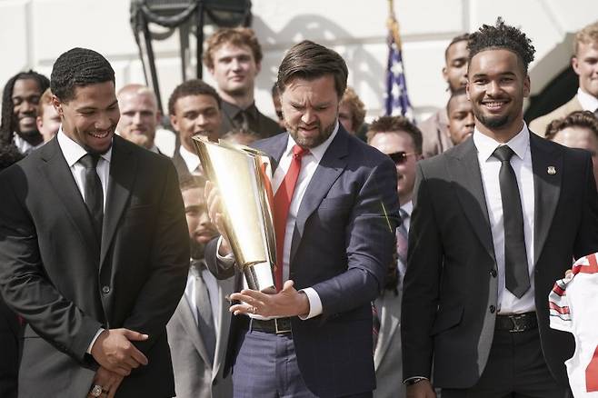 JD 밴스 미국 부통령(가운데)가 14일(현지시간) 미 워싱턴DC 백악관 정원에서 2025년 미 대학 미식축구 선수권 우승팀인 오하이오주립대의 선수들로부터 우승 트로피를 건네받고 있다.EPA연합뉴스