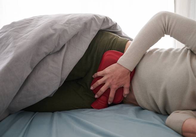A person holds a hot water compress to her lower abdomen while lying in bed.  (Getty Images)
