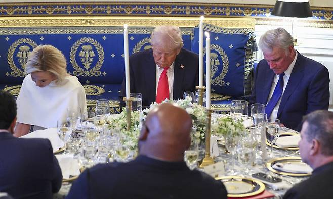 16일(현지시간) 미국 워싱턴 백악관 블루룸에서 열린 부활절 기도회 및 만찬 중 도널드 트럼프 대통령이 고개를 숙이고 기도하고 있다. 방 벽면과 식기, 촛대 등이 황금색으로 장식돼 있다. 워싱턴DC=AP연합뉴스