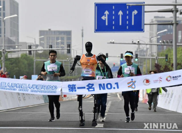 19일 중국 베이징 이좡 경제기술개발구에서 열린 휴머노이드 로봇 하프마라톤에서 우승한 로봇 '톈궁 울트라'가 참가팀 인원들과 함께 달리고 있다. (사진=신화/뉴시스)