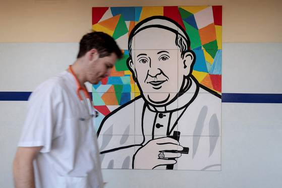 A man walks near a painting depicting Pope Francis at the Gemelli Hospital, where he is admitted for treatment, in Rome, Italy, March 3. [REUTERS/YONHAP]