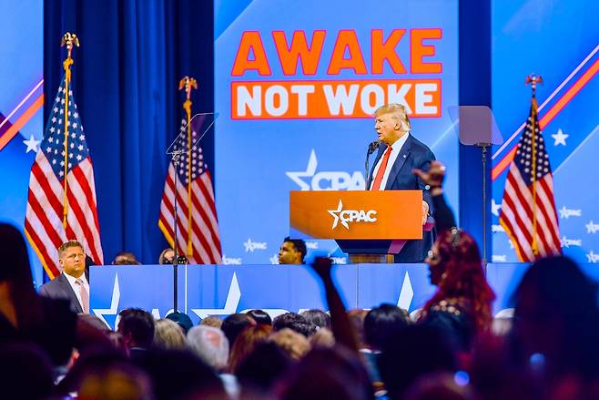 도널드 트럼프가 2022년 2월 미국 플로리다에서 열린 보수정치행동회의 행사 중 ‘Awake, not woke’ 슬로건 아래서 연설하고 있다. ‘진정으로 깨어 나라, 진보 쪽이 말하는 깨어있음(워크) 말고’ 정도로 해석할 수 있다. 출처: 위키미디어 공용