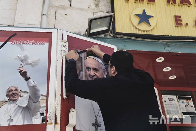 [베들레헴=AP/뉴시스] 프란치스코 교황이 선종한 21일  서안지구 베들레헴에서 한 상점 주인이 프란치스코 교황의 사진에 검은 리본을 달고 있다. 2025.04.21.