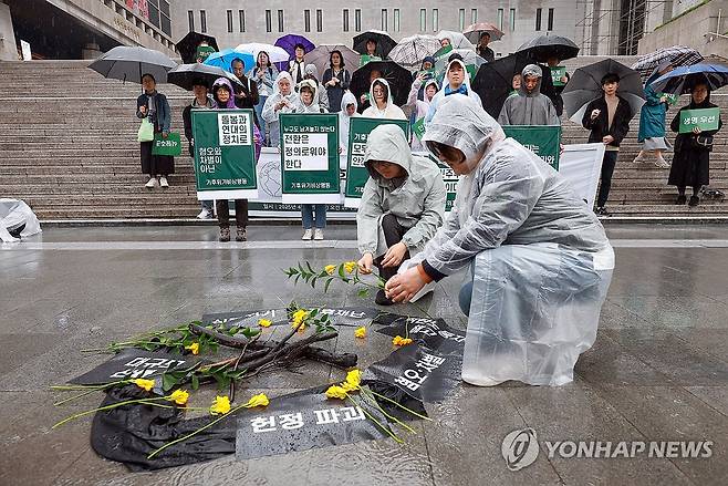 영남 산불에 불탄 나뭇가지 주변에 놓는 꽃 (서울=연합뉴스) 신현우 기자 = 지구의 날인 22일 서울 종로구 세종문화회관 계단에서 기후위기비상행동이 연 '기후재난과 민주주의 위기, 생명돌봄의 정치가 필요하다' 기자회견 참가자들이 영남 산불에 불탄 나뭇가지 주변으로 꽃을 놓고 있다. 2025.4.22 nowwego@yna.co.kr