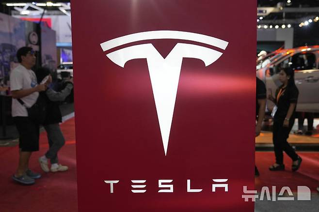 People pass by a Tesla sign at the Manila International Auto Show in Pasay city, Philippines Friday, April 11, 2025. (AP Photo/Aaron Favila)