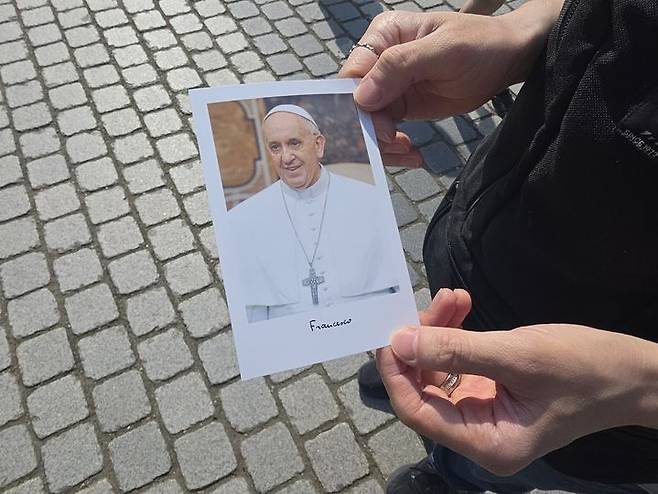 [서울=뉴시스] 고재은 수습기자 = 26일 오후 서울 종로구 명동성당 앞에서 한 추모객이 프란치스코 교황의 사진과 약력이 담긴 상본을 보여주고 있다. 2025.04.26. jeko@newsis.com *재판매 및 DB 금지