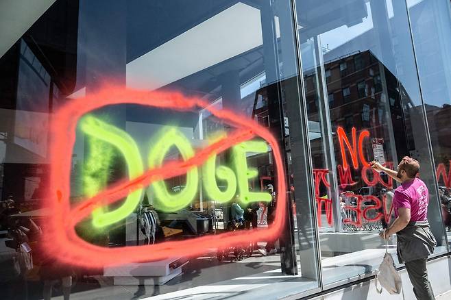 지난 22일(현지시간) 미국 뉴욕시의 한 테슬라 전시매장 유리창에 한 시민이 일론 머스크 테슬라 최고경영자(CEO)가 이끄는 트럼프 행정부의 정부효율부(DOGE)를 비판하는 낙서를 하고 있다. [AFP]