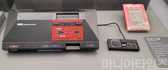 넷마블게임박물관. 1987년 발매된 '세가 마스터 시스템'. '세가 마크 III'와 성능은 대동소이 했다고 한다. FM 음원 및 3D 안경을 꽂을 수 있는 연결부를 내장한 것이 '세가 마크 III'와의 차이점이다. 게임기 오른쪽 하단에 보면 3D 안경 연결부가 보인다. 오른쪽은 '마이카드'형 게임 패키지로 발매된 '핏폴스'. 촬영 : 이동근 기자