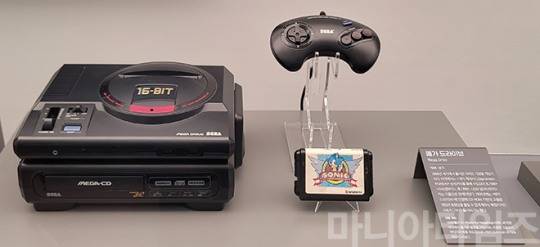넷마블게임박물관. 1988년 발매된 세가의 '메가 드라이브'와 '메가-CD', 오른쪽은 메가 드라이브용 게임 중 가장 많이 팔린 '소닉 더 헷지훅'. 메가 드라이브는 16비트 게임기 시대를 연 것으로 평가되며, 게임기에도 '16-BIT'라는 금색 각인이 보인다. 실제로 당시 게임기 중 가장 빠른 연산속도를 자랑해 액션 게임과 슈팅 게임에서 강세를 보였다. 그러나 경쟁 기기인 닌텐도의 '슈퍼 패미컴'에 비해 최대발색수가 적어 화면은 다소 거칠게 느껴졌으며, 서드파티 면에서 게임 발매수의 부족 등의 문제로 '슈퍼 패미콤'과의 경쟁에서 결국 밀렸다. 그러나 북미에서는 '슈퍼 패미컴' 보다 인기 있었다는 평가도 나오며 매니아들이 많다. 주변기기 중 사진에도 있는 '메가 CD' 외에 '메가 LD', '슈퍼 32X'가 있다. 메가 CD와 메가 LD는 대용량을 이용한 전용 게임이 있었으며, 기능이 향상되는 슈퍼 32X까지 연결하면 더 고사양 게임도 할 수 있었다. 그러나 메가 드라이브에 메가 CD, 슈퍼 32X까지 연결하면 모양도 모양이지만 3개 모두 별도의 전원을 연결해야 하고, 연결이 복잡해지기 때문에 '메가 타워' 라는 일종의 조롱석인 평가가 나오기도 했다. 따라서 세가에서도 이들을 모두 합친 일체형 기기 '넵튠'을 발매할 계획을 세웠으나 후계기인 '세가 새턴'이 나오면서 무산됐다. 참고로 이 넵튠이라는 명칭은 컴파일 하트의 '신차원게임 넵튠' 게임 시리즈에서 주인공 이름으로 사용된다. 매니아들이 많아 현재까지도 비라이센스 메가 드라이브용 게임이 나온다. 촬영 : 이동근 기자