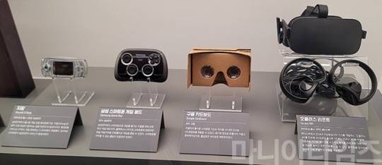 넷마블게임박물관. 왼쪽부터 삼성전자의 지팡 지원 게임폰(2005년 출시), 삼성 스마트폰 게임패드, 간이형 VR HMD(가상현실 헤드 마운트 디스플레이) '구글 카드보드', 오큘러스사(현 메타)의 본격 VR HMD 중 초기 모델인 '오큘러스 리프트'(2017년 출시). 지팡 지원 게임폰은 2005년 4월에 출시된 게임 특화 슬라이드폰으로 SKT 모델은 'SCH-G100', KTF 모델은 'SPH-G1000'으로 각각 '지백이', '지천이'로 불리웠다. 사진에는 '지팡'이라고 모델명 처럼 써 있는데, '지팡'은 KTF가 제공하는 모바일 게임 중 3D 가속칩이 탑재된 지팡 전용 휴대전화에서만 가능한 서비스를 뜻한다. 참고로 SKT에서도 비슷한 서비스 GXG를 제공했다. 지팡의 경우 무려 'KOEI 삼국지5', '팡야', '길티기어', '바이오하자드' 등 스마트폰 초기 수준의 게임들을 제공했으며, GXG도 '전차로 GO! 3D', 'SD건담 포켓제네레이션', '에반게리온 2' 등 다양한 게임을 제공했다. 해상도는 다소 떨어졌지만, 플레이스테이션, PC 등으로 출시된 게임을 컨버팅 한 것도 있었으니 게임 수준은 높은 편이었다. 구글 카드보드는 구글이 2014년 공개한 간이 VR HMD로 스마트폰을 넣으면 3D 영상이나 게임을 할 수 있었다. 소재는 골판지로 사실상 무료에 가까운 가격으로 배포했고, 도면도 무료로 배포했다. 촬영 : 이동근 기자