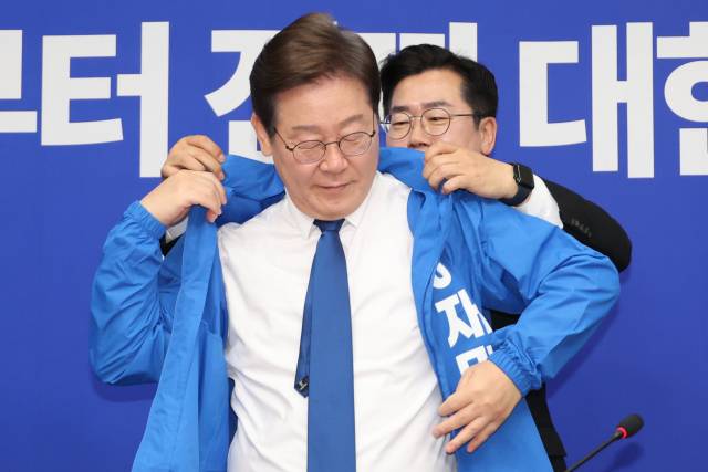 더불어민주당의 박찬대 당대표 직무대행 겸 원내대표가 28일 서울 여의도 국회에서 열린 최고위원회의에서 이재명 대선 후보에게 선거운동용 파란색 점퍼를 입혀주고 있다. 연합뉴스