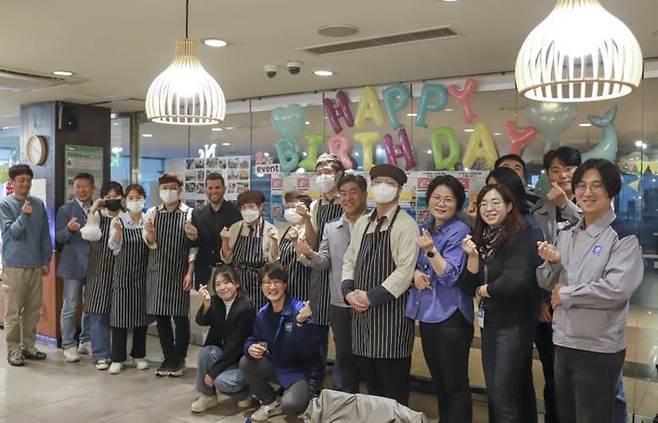 노틀담베이커리 오픈 2주년 축하 이벤트 기념 사진 촬영을 하고 있는 GM 한국사업장 임직원과 노틀담베이커리 직원 및 관계자. 사진=한국 GM제공