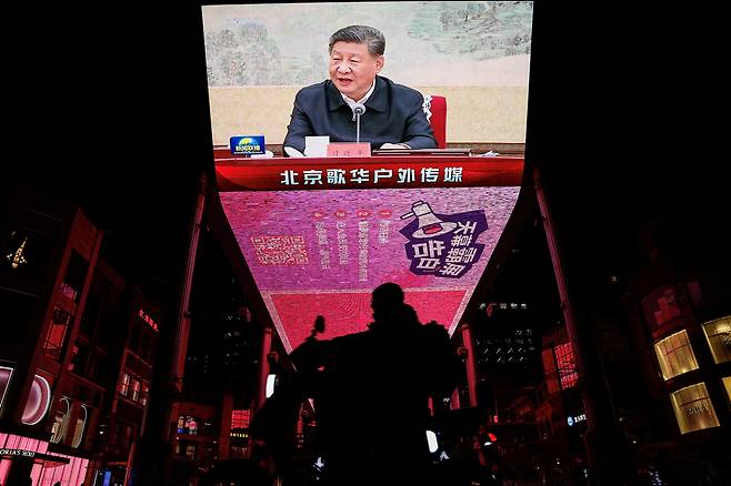 중국 베이징의 한 시내에서 지난해 연말 스쿠터를 타고 가는 시민 위로 시진핑 중국 국가주석의 모습이 방송으로 중계되고 있다. [로이터]