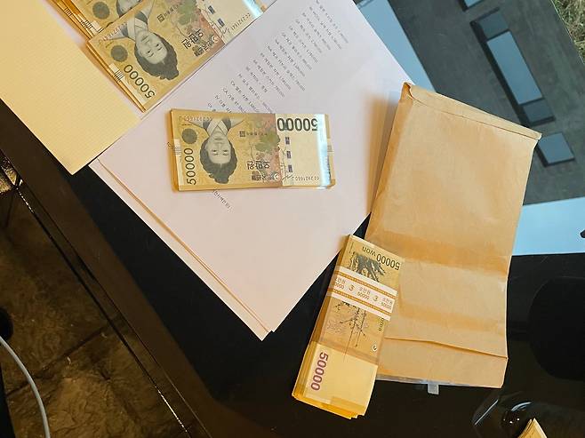 2021년 6월 문재인 전 대통령의 부인 김정숙 여사의 맞춤 의상 옷값으로 지불됐다는 현찰과 관봉권의 모습. A4 용지에는 김 여사가 구매해 간 것으로 추정되는 258만원 상당의 코트, 178만원 상당 자켓, 88만원 상당 슬렉스 등 제품명이 줄줄이 적혀 있다./본지 입수