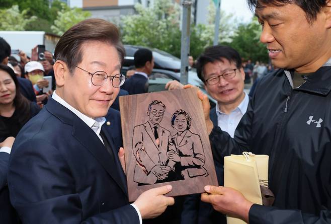 이재명 더불어민주당 대통령 후보가 청년 자산 형성, 일자리, 주거, 생활 안전망 전반에 걸친 종합 대책을 발표했다.사진은 이 후보가 2차 골목골목 경청투어에 나선 지난 5일 오후 충북 진천군의 혁신도시 상가를 찾아 한 시민으로부터 이 후보와 김혜경 여사를 나무판에 각인한 그림판을 선물 받던 모습. /사진=뉴스1