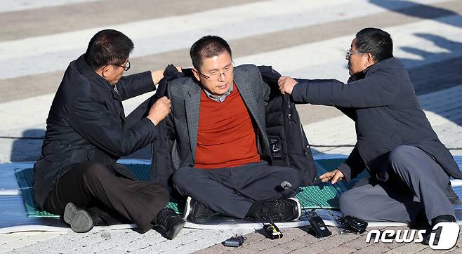 황교안 자유한국당 대표가 20일 오후 서울 종로구 청와대 사랑채 인근에서 지소미아 파기·패스트트랙 법안 강행 처리 등 철회, 문재인 정부의 실정에 따른 국정 대전환을 촉구하며 단식농성을 시작하고 있다. 김문수(왼쪽) 전 경기지사, 차명진 전 의원의 도움 받아 외투 입는 황교안 대표. 2019.11.20/뉴스1 ⓒ News1 이동해 기자