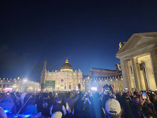 7일(현지시간) 바티칸 성 베드로 광장에 모인 사람들이 시스티나 성당 굴뚝에서 나오는 검은 연기를 지켜보며 촬영하고 있다. /연합뉴스