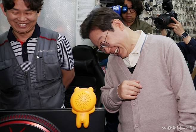 [칠곡=뉴시스] 조성우 기자 = 민심을 청취하는 '경청 투어'에 나선 이재명 더불어민주당 대선후보가 9일 경북 칠곡군 석적읍 인근 한 열쇠가게에서 한 도장가게에서 자신의 유세 모습을 실시간으로 보고 있던 상인의 모니터를 보고 활짝 웃고 있다. 2025.05.09. xconfind@newsis.com /사진=조성우