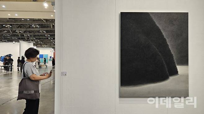 ‘아트부산 2025’ 전경. 한 관람객이 김보희 작가의 ‘투워즈’ 연작이 걸린 갤러리현대 부스를 찬찬히 돌아봤다. 앞쪽으로 김 작가의 신작 ‘투워즈’(2025, 162×130㎝)가 보인다. 시그니처인 초록을 거둔 자리에 짙은 무채색을 쓴 신작 여러 점을 포함, 출품한 김 작가의 12점 모두가 판매됐다(사진=오현주 문화전문기자).