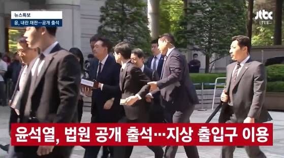 내란 우두머리 혐의로 재판을 받는 윤석열 전 대통령이 12일 법원에 공개 출석하는 과정에서 경호원이 질문하는 취재진의 팔을 잡아끌어 제지하고 있다. 〈사진=JTBC 방송화면 캡처〉