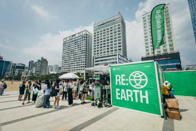 롯데백화점이 2024년 8월 부산 광안리해수욕장에 마련한 '리얼스 마켓(RE:EARTH MARKET)'에 참가자들이 줄을 서있다. 이 회사가 주관하는 '플로깅(Plogging·조깅하며 쓰레기 줍기)'의 베이스 캠프 역할을 하는 곳이다. 롯데백화점 제공