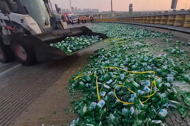 13일 오후&nbsp;5시43분쯤 전북 완주군 익산-장수 고속도로 완주나들목에서 장수 방향으로 진입하던 17t 윙바디 화물차에서 소주병 1만5000여개가 도로에 쏟아지는 사고가 나자 한국도로공사가 중장비를 동원해 깨진 병을 치우고 있다. 독자 제공