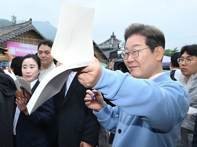 이재명 더불어민주당 대통령 후보가 15일 경남 하동군 화개장터 노래비 앞에서 배우자 김혜경 여사의 저서 ‘밥을 지어요’에 서명하고 있다. 공동취재사진