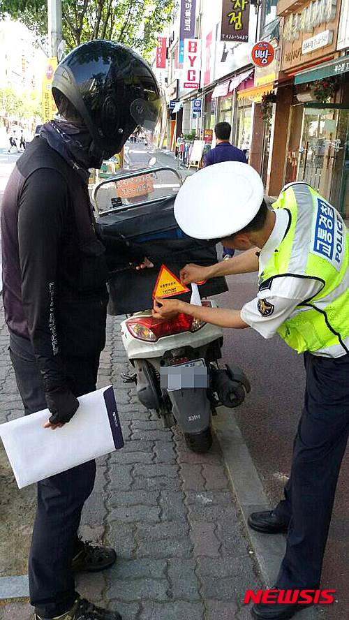 [대전=뉴시스]문승현 기자 = 대전서부경찰서 소속 교통경찰관이 배달용 이륜차에 교통법규준수를 강조하는 반사스티커를 붙여주고 있다. 경찰은 이와 함께 이륜차 운전자의 난폭운전이나 안전모 미착용행위 등을 집중 단속할 방침이다. 2015.06.04. (사진=대전지방경찰청 제공) photo@newsis.com