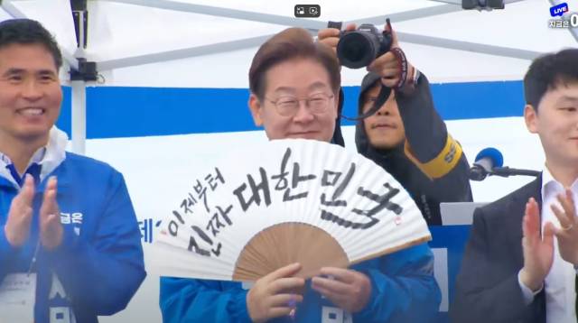 ▲16일 전북대 후문 앞에서 펼쳐진 전주유세에서 더불어민주당 이재명 대선후보가 전주 한지로 만들어진 부채에 '이제부터 진짜 대한민국'이라는 글씨가 써진 부채를 선물받고 기념사진을 촬영하고 있다. 이재명 후보는 호남권 재생에너지사업 벨트를 강조하면서 RE100을 모르는 사람이 '아윌백(I'll back)'을 얘기하고 있다며 '아윌백'은 안된다고 말해 청중들의 호응을 유도했다. ⓒ