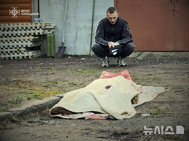 [AP/뉴시스] 18일 우크라 비상대처부 제공 사진으로 러시아 드론 공격에 사망한 시신 앞에 한 남성이 쪼구리고 앉아있다