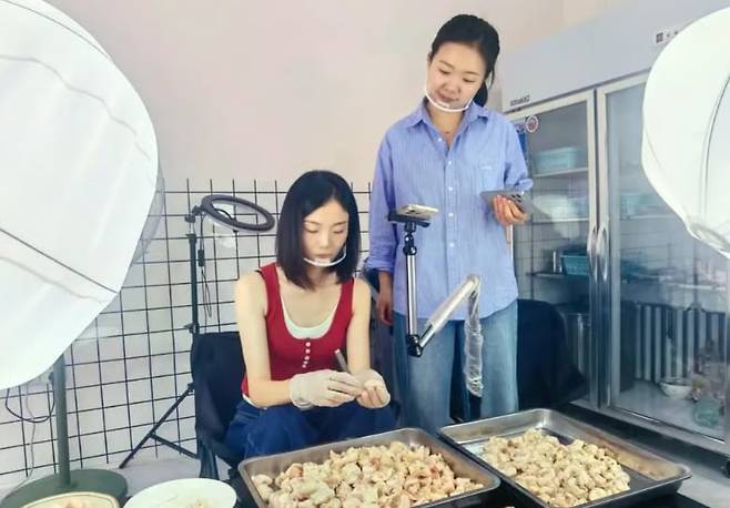 닭고기를 손질하는 영상을 촬영 중인 왕위셴(왼쪽)의 모습. /SCMP