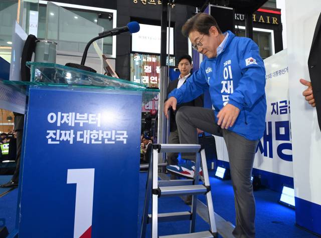 이재명 더불어민주당 대선 후보가 제21대 대통령선거 재외국민투표가 시작된 20일 경기 김포시 구래역 문화의 거리에서 유세를 하며 뒷열에서 자신이 잘 보이지 않는 시민들에게 인사하기 위해 갑자기 연단에 있던 취재진의 사다리에 오르고 있다.김포=오승현 기자 2025.05.20