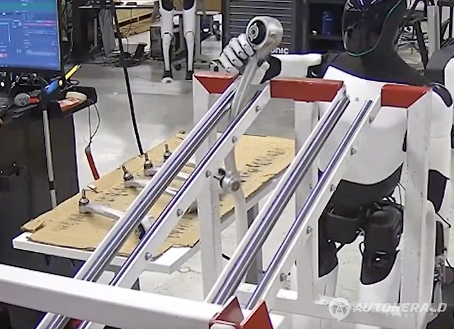 테슬라 옵티머스가 모델 X의 서스펜션 부품(포어 링크)을 들어 운반하는 장면 (테슬라 공식 X 캡처)