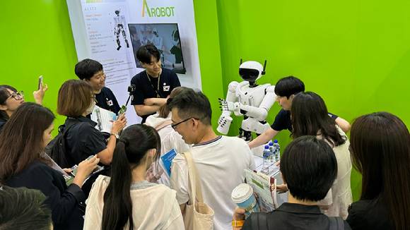 에이로봇의 휴머노이드 로봇 '엘리스'가 21일 컴퓨텍스 2025에서 관람객들과 주사위 놀이 후 물을 건네주고 있다. [사진=에이로봇]