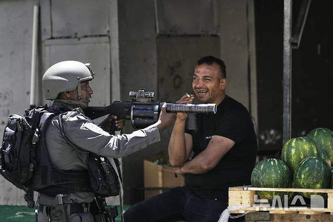 [나블루스=AP/뉴시스]이스라엘군은 21일(현지 시간) 요르단강 서안을 방문한 유럽 외교관들에게 경고 사격을 했다가 사과했다. 사진은 20일 요르단강 서안지구 나블루스 인근 아스카르 난민캠프에서 이스라엘군의 기습 작전이 벌어진 가운데, 한 이스라엘 국경 경찰이 수박 노점 옆에 자리를 잡고 있는 모습. 2025.05.22.