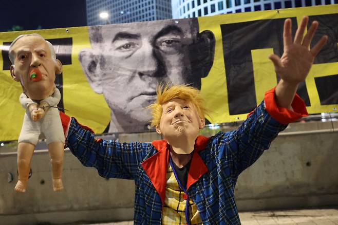 10일(현지시간) 텔아비브에 있는 이스라엘 국방부 앞에서 한 시위자가 도널드 트럼프 미국 대통령을 형상화한 가면을 쓰고, 베냐민 네타냐후 이스라엘 총리를 묘사한 가면을 씌운 인형을 들고 반정부 시위에 참여하고 있다. 이 시위는 전쟁 종식과 2023년 10월 7일 하마스 무장세력의 공격 이후 가자지구에 억류된 이스라엘 인질들의 석방을 촉구하기 위해 열렸다. 해당 사진과 기사 내용은 직접적 연관성이 없다.(사진=AFP)