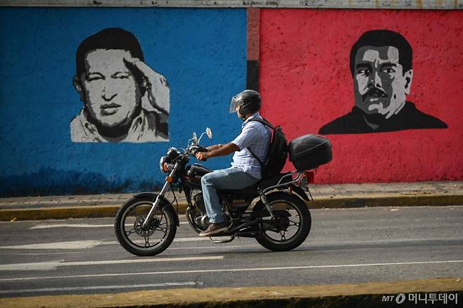 지난해 9월 26일 한 바이커가 우고 차베스 전 대통령과 니콜라스 마두로 현 대통령의 벽화가 그려져 있는 카라카스 거리를 달리고 있다. 대선 결과를 둘러싼 정정 불안이 지속되는 가운데 공식 달러 환율과 암시장 시세간 차가 점차 커지며 이전의 고(高)인플레이션 사태가 재연될 우려가 커지고 있다. /AFPBBNews=뉴스1