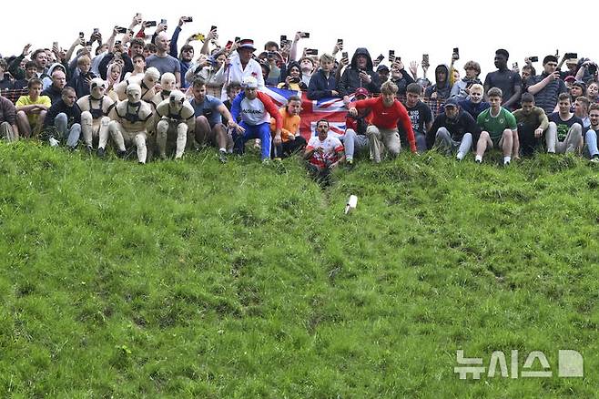 [브록워스=AP/뉴시스] 26일(현지 시간) 영국 글로스터셔주 브록워스의 쿠퍼스 힐에서 연례  치즈 굴리기 대회가 열려 남자부 참가자들이 언덕을 굴러 내려오고 있다. 이 대회는 약 180m 거리의 가파른 언덕에서 구르는 치즈를 잡아 결승선에 먼저 들어오는 사람이 우승하는 경기이다. 2025.05.27.