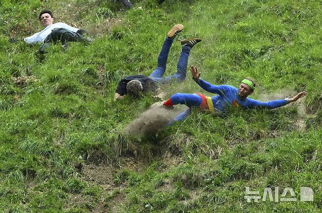 [브록워스=AP/뉴시스] 26일(현지 시간) 영국 글로스터셔주 브록워스의 쿠퍼스 힐에서 연례  치즈 굴리기 대회가 열려 남자부 참가자들이 언덕을 굴러 내려오고 있다. 이 대회는 약 180m 거리의 가파른 언덕에서 구르는 치즈를 잡아 결승선에 먼저 들어오는 사람이 우승하는 경기이다. 2025.05.27.