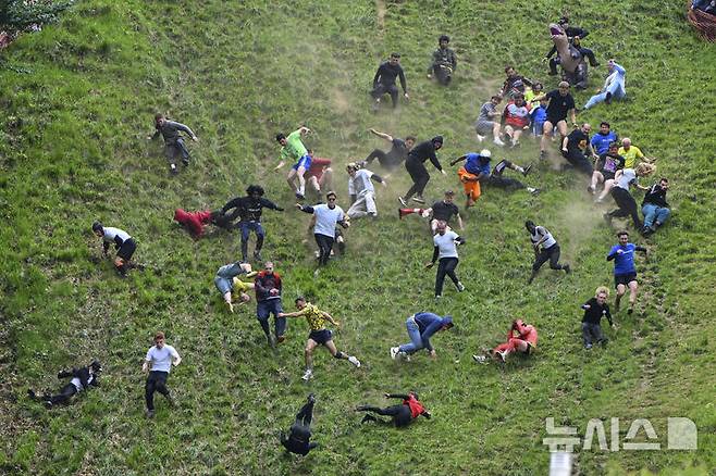 [브록워스=AP/뉴시스] 26일(현지 시간) 영국 글로스터셔주 브록워스의 쿠퍼스 힐에서 연례  치즈 굴리기 대회가 열려 남자부 참가자들이 언덕을 굴러 내려오고 있다. 이 대회는 약 180m 거리의 가파른 언덕에서 구르는 치즈를 잡아 결승선에 먼저 들어오는 사람이 우승하는 경기이다. 2025.05.27.
