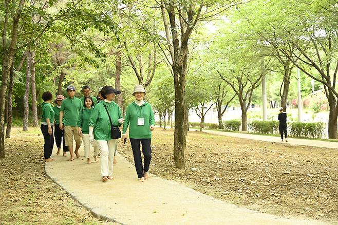 달성군 창리공원 맨발산책로를 걷고 있는 주민들. 초록빛 숲속에서 신발을 벗고 걷는 시민들의 표정이 밝다. <달성군 제공>