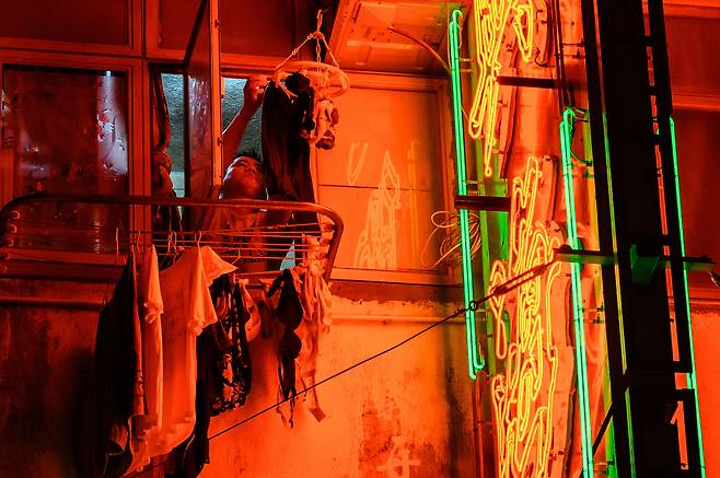 A man hangs laundry next to a lit neon sign outside the window of his flat in Hong Kong on Nov. 18, 2024. [AFP/YONHAP]