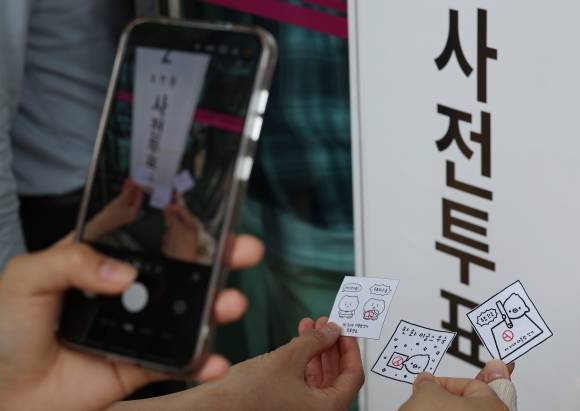 제21대 대통령선거 사전투표 첫날인 29일 서울 강남구 삼성2동주민센터에 마련된 사전투표소 앞에서 시민들이 투표 도장이 찍힌 그림을 들고 기념 촬영을 하고 있다. 2025.5.29 연합뉴스