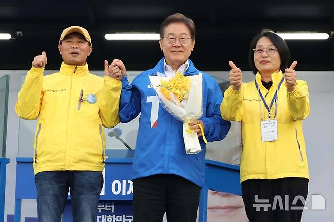 [안산=뉴시스] 조성봉 기자 =  이재명 더불어민주당 대선 후보가 24일 경기 안산 단원구 안산문화광장에서  열린 유세에서 세월호 유가족에게 꽃을 선물받고 함께 시민들에게 인사하고 있다. 2025.05.24.suncho21@newsis.com