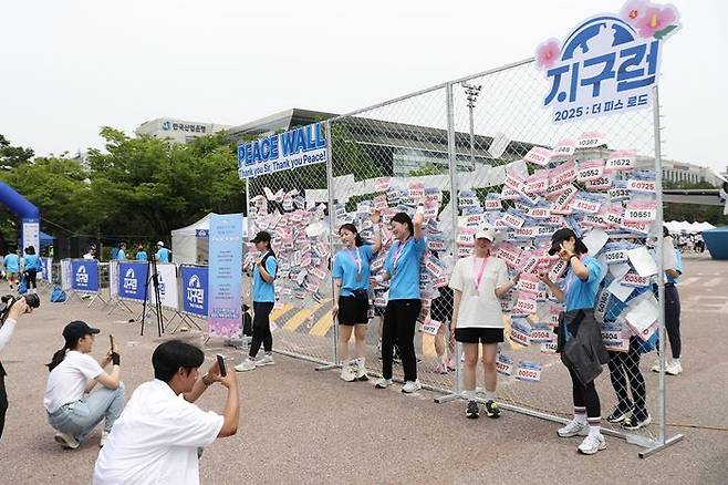 ▲‘2025 지구런 : 더 피스 로드’ 참가자들이 완주 후 ‘피스 월(PEACE WALL)’ 포토존에서 기념촬영을 하고 있다. (사진제공=지구런)