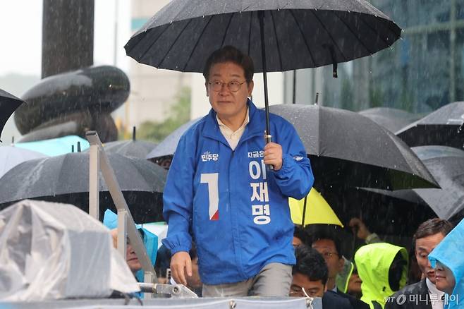 [순천=뉴시스] 이재명 더불어민주당 대선 후보가 15일 전남 순천 연향동 패션의거리에서 열린 유세에서 우산을 쓰고 단상에 오르고 있다. 2025.05.15.