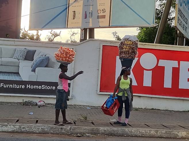 가나 수도 아크라의 길거리 행상 가나 아크라 도심 도로에 차가 막히면 정차된 차 사이로 행상들이 아슬아슬하게 다닌다. 무게중심을 잡고 무거운 간식과 음료 등을 가득 담은 대야를 머리에 이고 뛰다시피 한다.
[이현정 제공. 재판매 및 DB 금지]